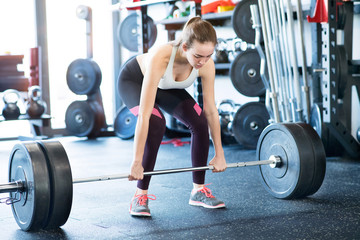 Beautiful young fit woman in gym lifting heavy barbell