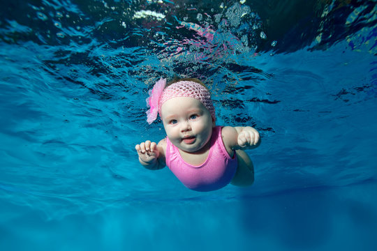 Baby in a pink dress swims underwater on a blue background. Portrait. Landscape orientation.