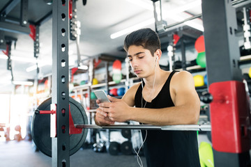 Fototapeta na wymiar Hispanic man in gym resting, holding smart phone,listening music