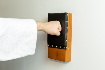Karate master punching with knuckles an okinawan japanese traditional makiwara wood board wearing a white dogi