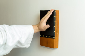 Karate master hitting with an open hand a japanese traditional makiwara wood board wearing a white kimono