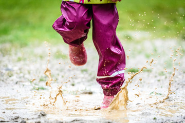 Children in rubber boots and rain clothes jumping in puddle.
