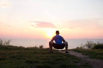 Young male stretching before fitness training session at the park. Healthy young man warming up outdoors. Sunset or sunrise in the sea or ocen on background