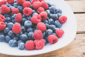 Himbeeren und Blaubeeren auf einem weißen Teller vor Holz Hintergrund