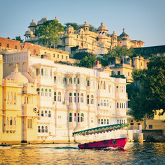 Naklejka premium Water view of City Palace in Udaipur City Of Lakes in Rajastan, India. Red boat on Pichola Lake in Udaipur