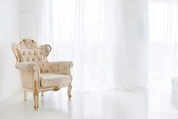Vintage armchair against big windows with curtains in white interior