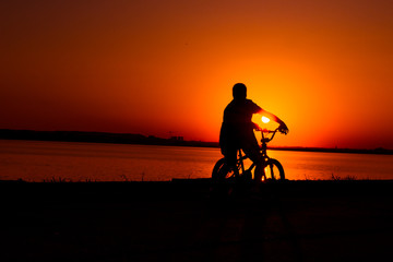 Silhouette of man biker cycling by the lake at sunset