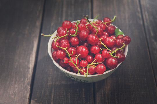 Red currants in bowl on rustic wood background, closeup