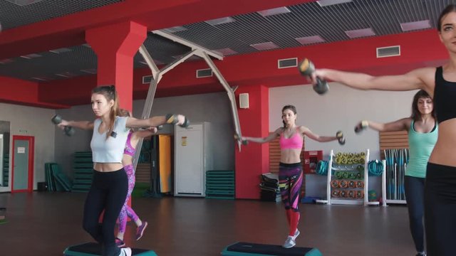 Aerobics class stepping together led by instructor and lifting dumbbells at the gym