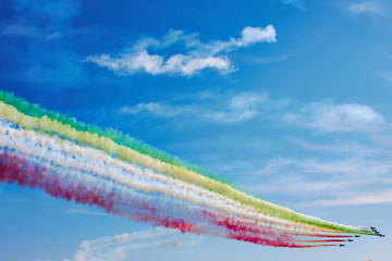 Air fighters on an air show flying in the shape of a geometric figure with colorful bright trails of smoke against a blue sky with clouds. Air performance