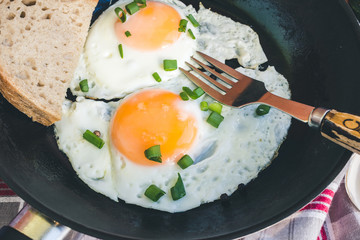 Fried eggs on pan with fork and bread on napkin