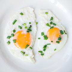 Fried eggs with green onion in white plate, close-up, top view