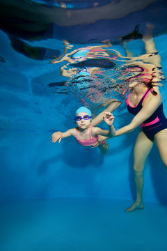 Mom learns to swim underwater a little girl in a pink swimsuit. Portrait. Shooting under water. Vertical view.