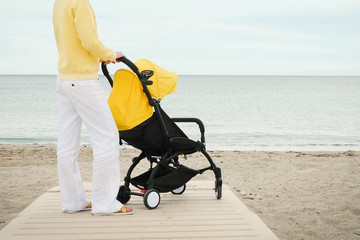 Young mother walking with baby stroller at the beach