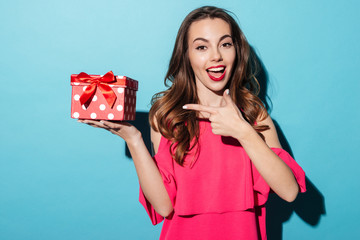 Smiling girl in dress pointing finger at a gift box