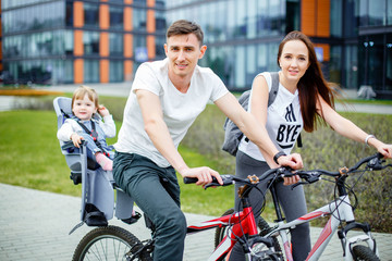 Obraz premium Young parents ride a bicycle with a small daughter on city streets