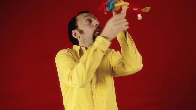 A grownup man having fun playing with a plane toy. Funny scene.
