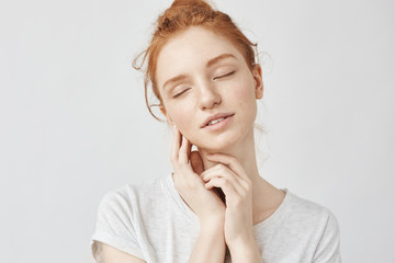 Portrait of tender girl with foxy hair and closed eyes smiling.