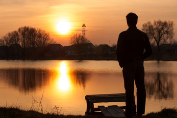 Man silhouette, standing on river stones gangway and contemplating a beautiful sunset.