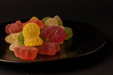 Close-Up Of Colorful Candy. mixed fruit flavoured jellies on a black plate