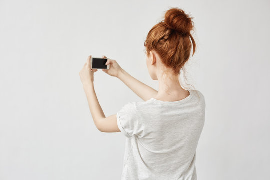 Beautiful redhead girl holding phone standing back to camera.