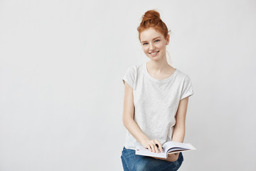 Beautiful ginger student girl smiling holding book looking at camera.