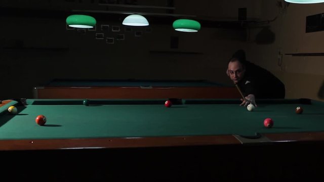 Man playing pool in the dark billiard club. Player performs trick shot and throws pink ball in the middle hole. American billiard, 9-ball, nine-ball pool.