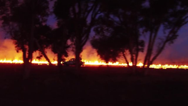 A 4k tracking shot of a ute or small truck monitoring the fire on a farming rural property as they are burning off at dusk in Australia.