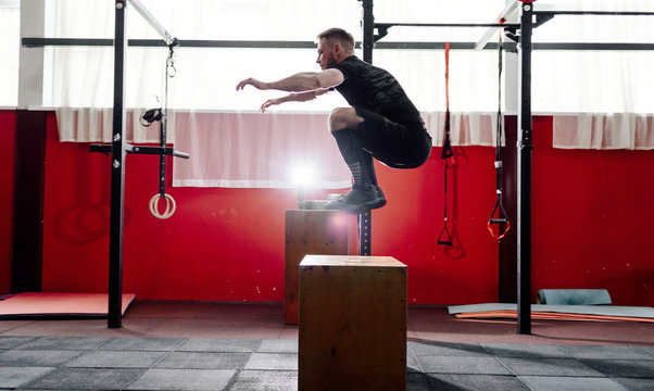 Fit young man jumping onto a box as part of exercise routine. Man doing box jump in the gym. Athlete is performing box jumps