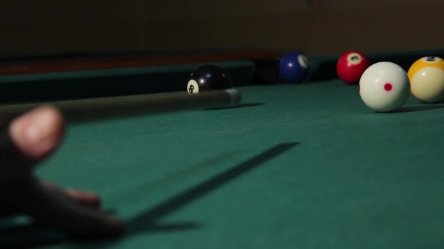 Billiards game. Player with the stick strikes the cue ball and it hits blue ball that goes in the hole, close up. American billiard, 9-ball, nine-ball pool.
