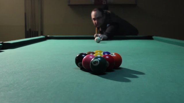 Man performs first shot in billiard game, Player smashing balls on green pool table. American billiard, 9-ball, nine-ball pool.