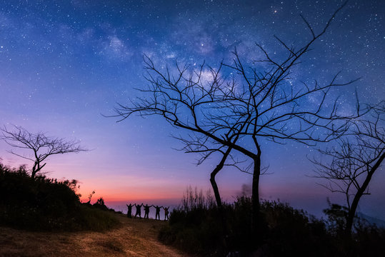 Milky Way.Night sky with stars and silhouette of standing happy peoples raised up arms. Blue milky way with people on the mountain.Background with universe. Night landscape. Travel freedom concept.