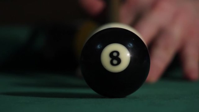 Billiard player hitting cue ball and white ball hit black ball. Black ball goes in the hole and white ball moving back and put yellow ball in second middle hole. Trick shot.
