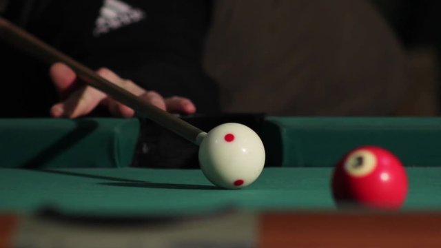 Man playing billiard in dark bar pool room. Player hitting the cue ball and she hit red ball, but misses the hole. Ball does not go in hole. American billiard, 9-ball, nine-ball pool.
