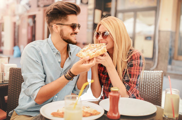 Beautiful young couple sitting in the cafe and eating pizza. Consumerism, food, lifestyle concept