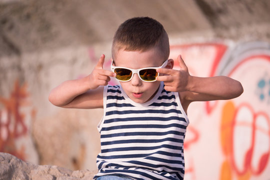 Funny small boy in sunglasses and shirt on graffiti wall background