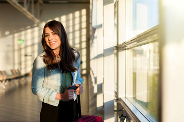 Fototapeta na wymiar Woman smiling waiting her flight at airport terminal waiting room with her trolley bag.