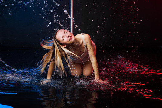 A young beautiful European woman in a photo studio with water is engaged in half-dancing with pole vaults