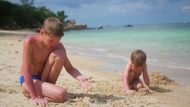 a young man plays with child on the beach. To make the sand molds