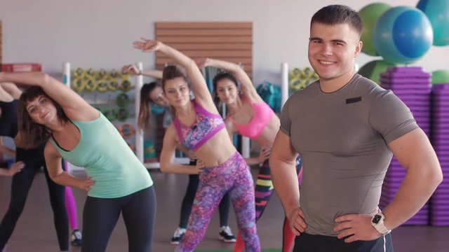 Close-up of male fitness trainer. He looks at a group of girls who train in an aerobic gym