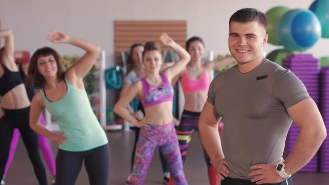 Close-up of male fitness trainer. He looks at a group of girls who train in an aerobic gym