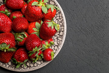 fresh ripe useful fruit strawberry in a clay bowl closeup on a black background
