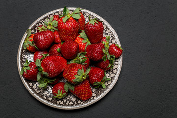 fresh ripe useful fruit strawberry in a clay bowl closeup on a black background