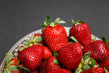 fresh ripe useful fruit strawberry in a clay bowl closeup on a black background