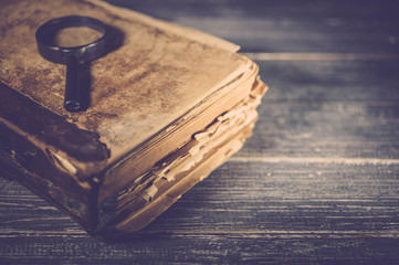 Old brown book and magnifying glass on tree background. Close up. Vintage toning. Selective focus.