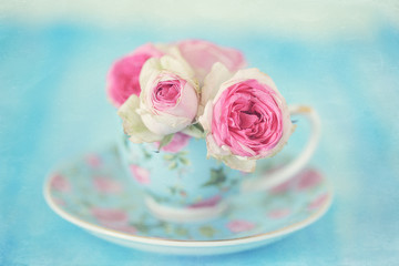 Obraz na płótnie Canvas Pink roses in a beautiful tea bowl on a blue background.