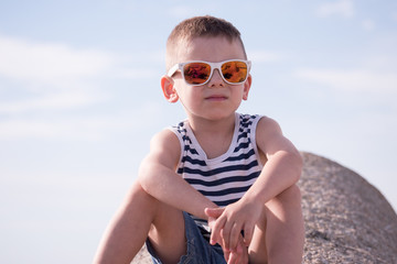 cute small boy with sunglasses, vest , shorts against the sky