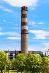 Obraz premium a high concrete chimney on the background of beautiful sky with clouds and bright spring greens