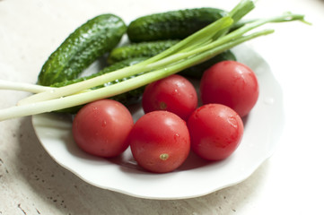 Fresh organic tomatoes and cucumbers with green onions on a white plate