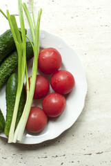 Fresh organic tomatoes and cucumbers with green onions on a white plate